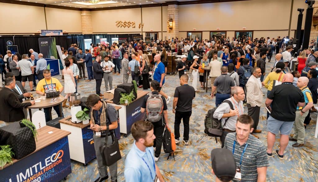 Large group of people at a business conference or expo, mingling and visiting exhibitor booths in a spacious, well-lit event hall.