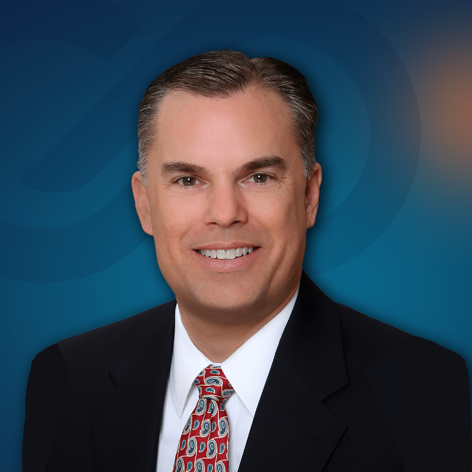 A man in a suit and patterned tie smiling at the camera, with a blue gradient background featuring a subtle abstract design.
